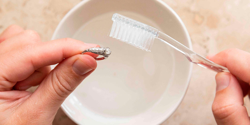 Pessoa com um anel de prata em uma das mãos e na outra segurando uma escova de dentes. 